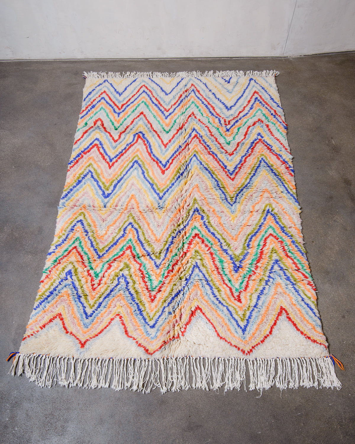 Berberlin Finest Rug made of plush cream wool with a colourful zigzag design laying flat on concrete floor.